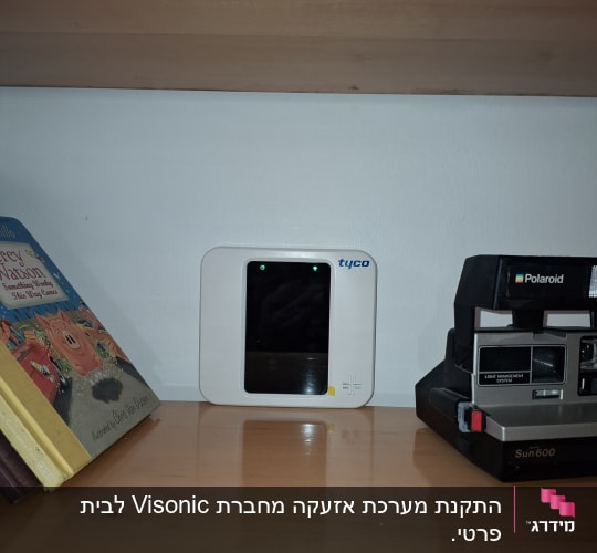 מכשיר אבטחה לבן עם מסך קטן על מדף עץ